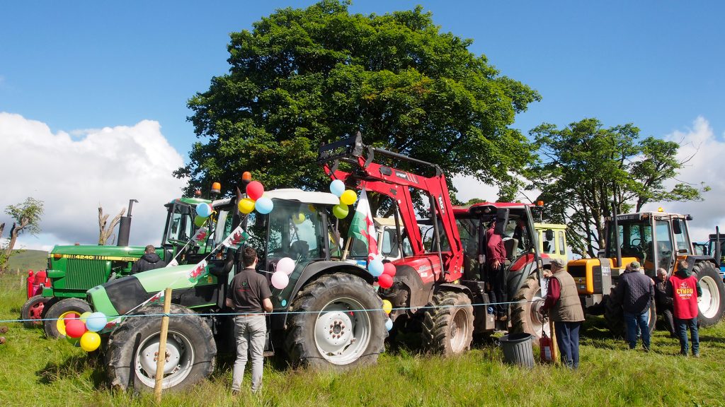 Several tractors lined up in a field with drivers talking outside the cabins