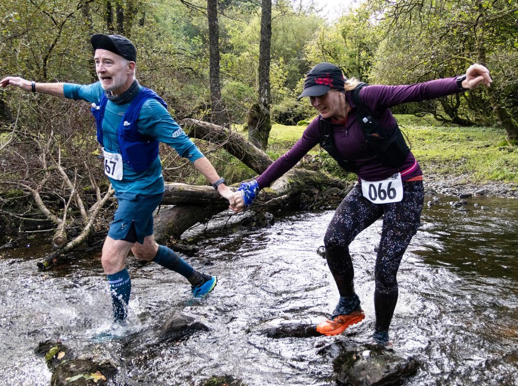 Male and female runners crossing a stream holding hands